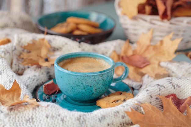 Bufanda de punto blanca taza azul de galletas de café y hojas amarillas secas