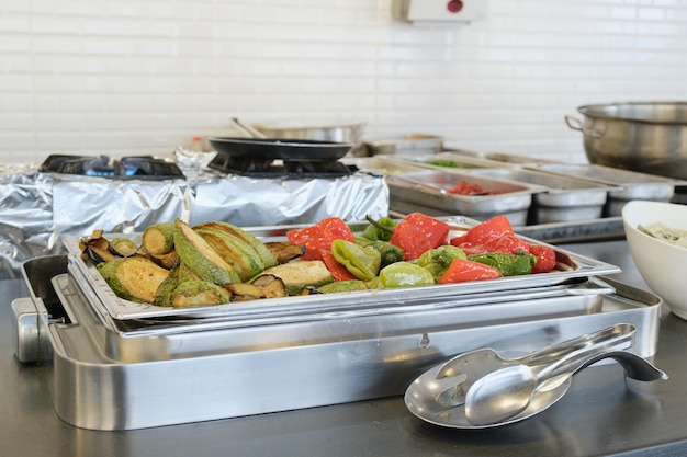 Buffet com recipiente de metal para pratos quentes com abobrinha grelhada e pimentão