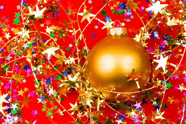 Bugiganga de Natal dourada com enfeites em forma de estrela sobre fundo vermelho