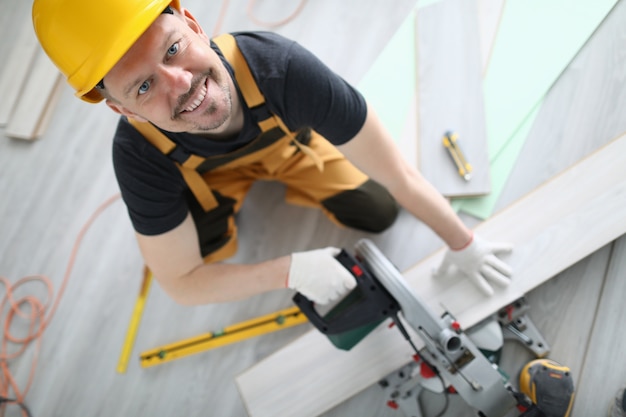 Builder em macacão e capacete com corte laminado na máquina na sala.