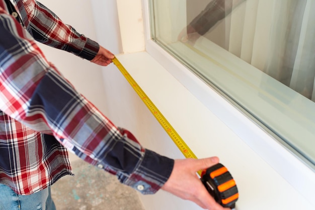 Builderrepairman misst die Länge der installierten Fensterbank in Nahaufnahme