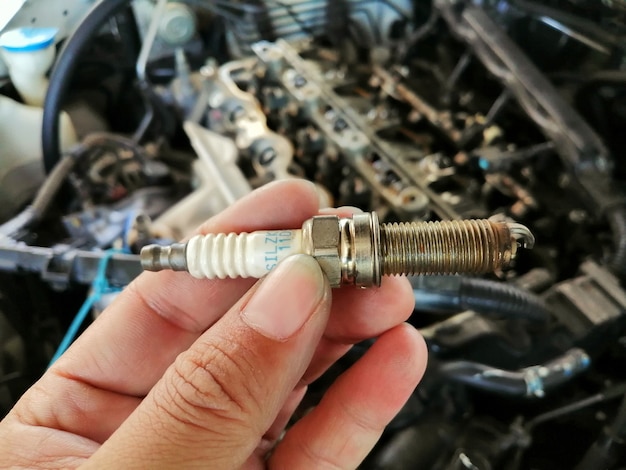 Bujía de coche de iridio en la mano del mecánico con motor de coche fondo borroso en el garaje de reparación