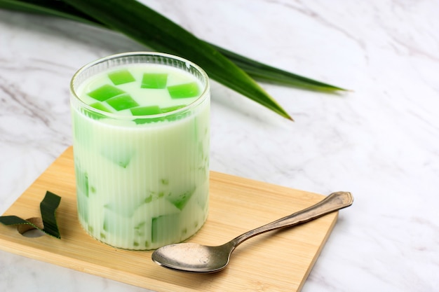 Buko Pandan es un alimento dulce elaborado con gelatina y jugo de pandan con perlas de sagú y pulpa de coco rallada con crema o leche. Servido en una mesa de cristal, fondo blanco con espacio de copia.