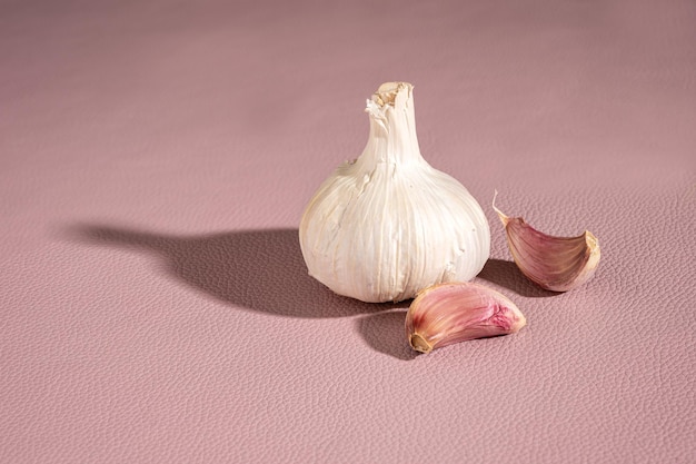 Bulbo de alho roxo e dentes de alho em fundo rosa