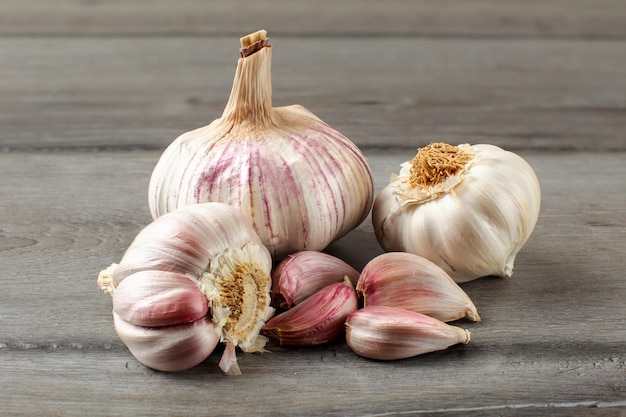 Bulbos de ajo, con algunos dientes morados sobre una mesa de madera gris.