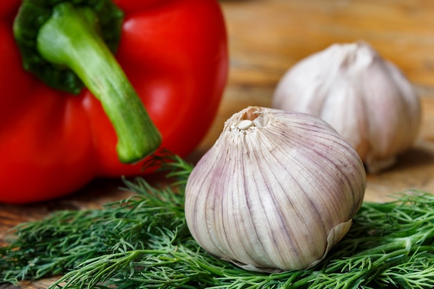 Bulbos de ajo, eneldo fresco y pimientos dulces en una mesa de madera