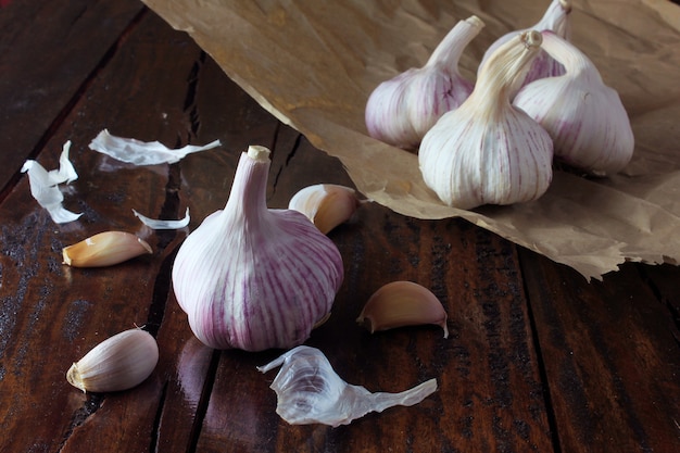 Bulbos de alho no papel de embalagem, na mesa de madeira rústica