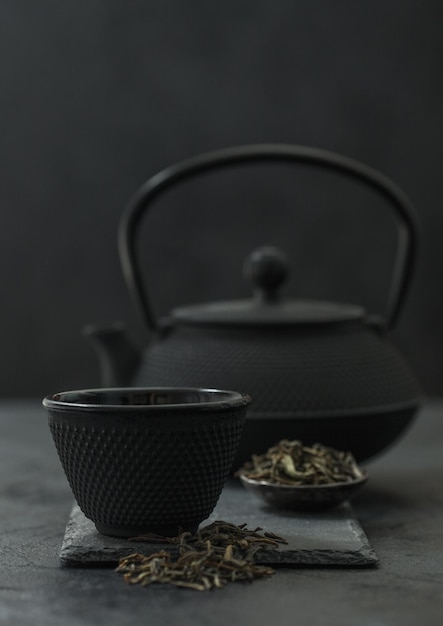 Bule chinês com prato de chá preto solto e xícara em fundo preto