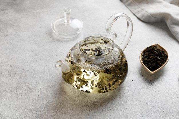 Bule com folhas de chá de ervas verdes em um fundo cinza em uma mesa com um guardanapo. Bule quente.