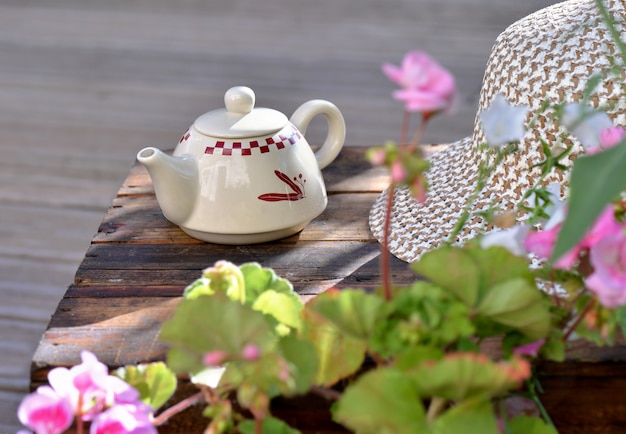 bule de chá em uma mesa de madeira em um terraço com flores e chapéu