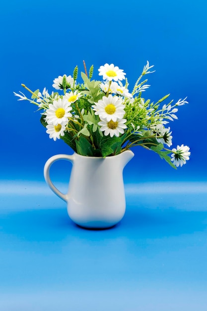 Bule de vaso com flores de plástico sobre fundo azul