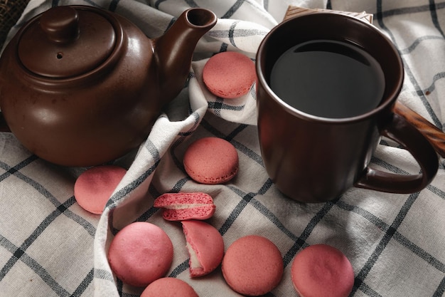 Bule e xícara em pano de cozinha com macarons rosa dispersos