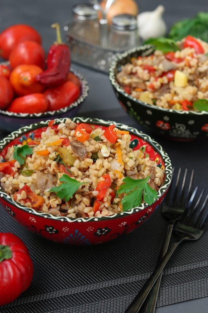 Bulgur com cogumelos e legumes em duas tigelas em um prato oriental vegetariano de fundo escuro