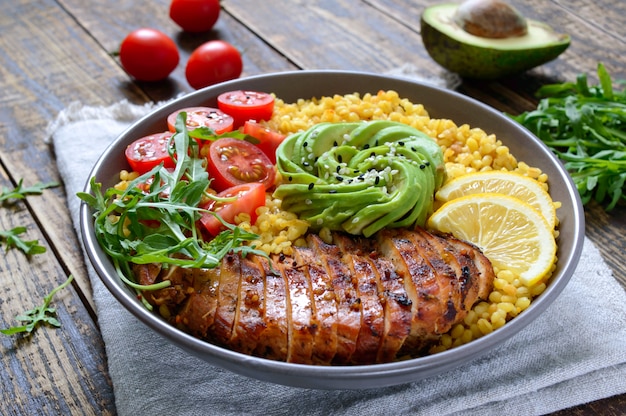 Bulgur com peito de frango grelhado, legumes frescos, abacate, rúcula. Faça dieta o almoço em uma mesa de madeira. Comida saudável