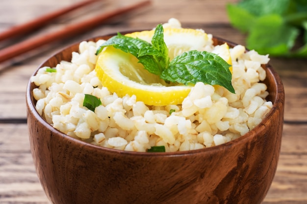 Bulgur cozido com limão fresco e hortelã em um prato. Um prato oriental tradicional chamado Tabouleh. superfície de madeira rústica