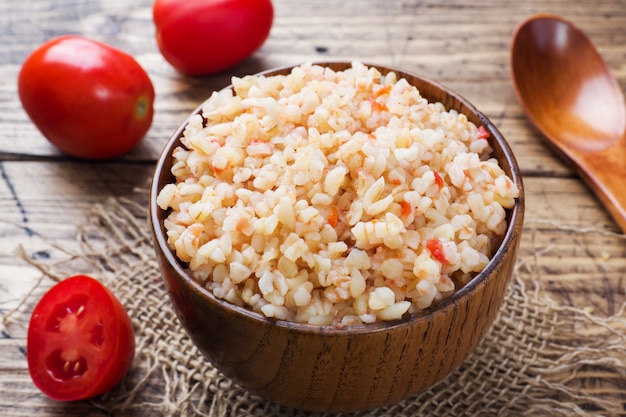 Bulgur cozido com tomates em uma tigela de madeira.