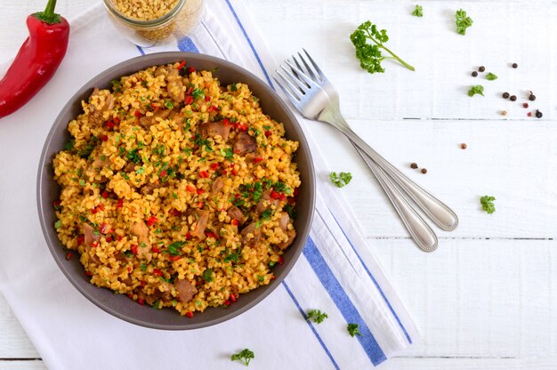 Bulgur delicioso con verduras, carne y verduras en una mesa de madera blanca. Menú dietético Nutrición apropiada. Vista superior.