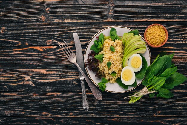 Bulgur con espinacas de aguacate y huevo cocido Sobre un fondo de madera Vista superior Espacio de copia