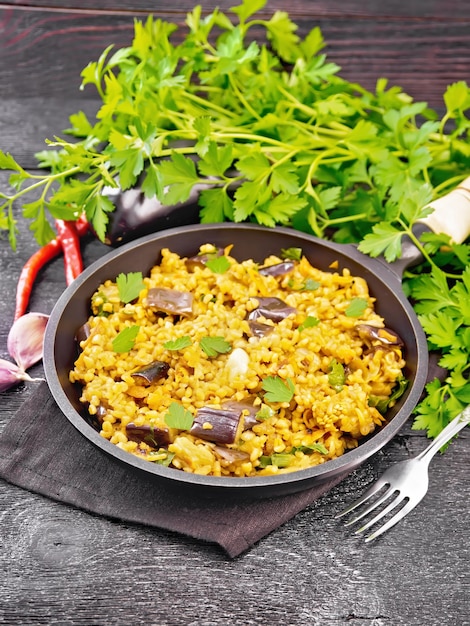 Bulgur guisado con berenjenas, zanahorias, ajo y cebolla en una sartén sobre una servilleta sobre fondo de tablero de madera