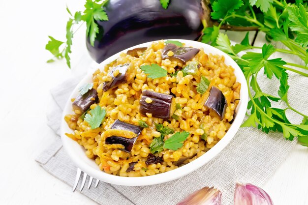 Bulgur guisado com berinjela cenoura alho e cebola em uma tigela sobre uma toalha no contexto da placa de madeira clara