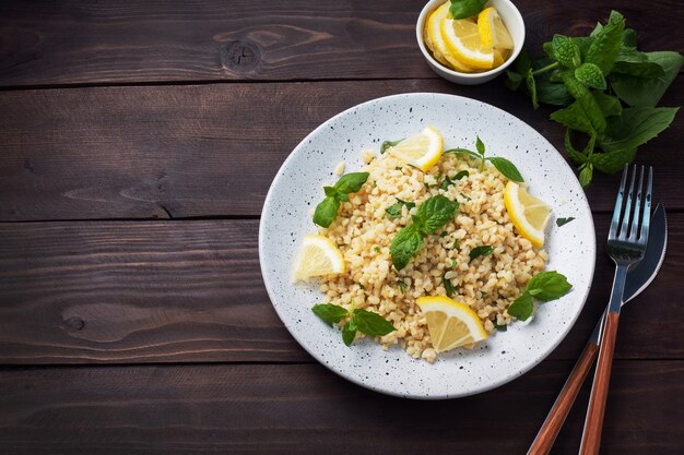 Bulgur hervido con limón fresco y menta en un plato. Un plato oriental tradicional llamado Tabouleh. fondo de madera oscura. vista superior, espacio de copia