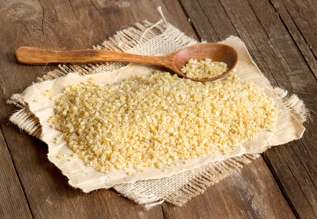 Bulgur orgânico cru com uma colher em uma mesa de madeira fechar