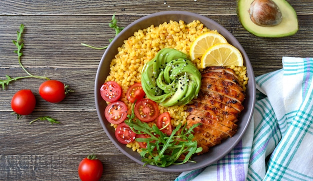 Bulgur con pechuga de pollo a la parrilla, verduras frescas, aguacate, rúcula. Almuerzo de dieta en una mesa de madera. Comida sana. Vista superior.