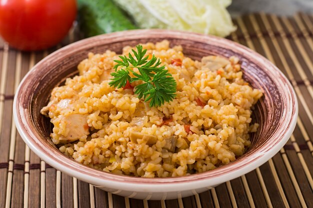 Bulgur picante con champiñones y pollo en cuenco de cerámica. Papilla de Oriente popular.