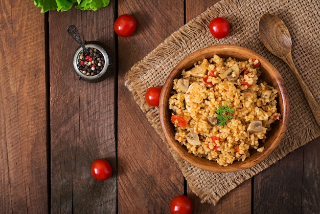 Bulgur con pollo, setas y tomates en un tazón de madera.