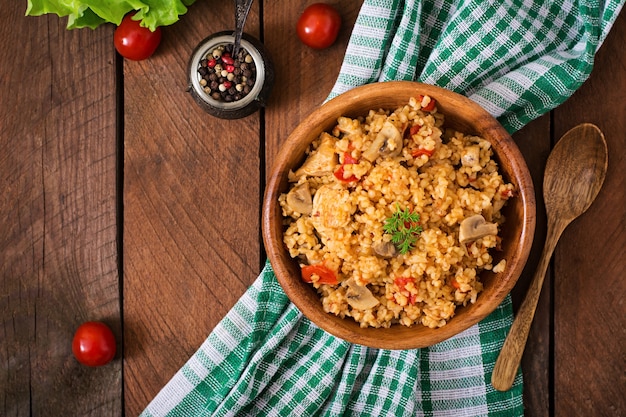 Bulgur con pollo, setas y tomates en un tazón de madera.