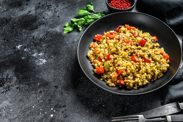 Bulgur con verduras y carne en un plato. Fondo negro.