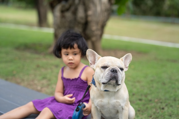 Bulldog francés sentado en un banco con niña vestida de violeta