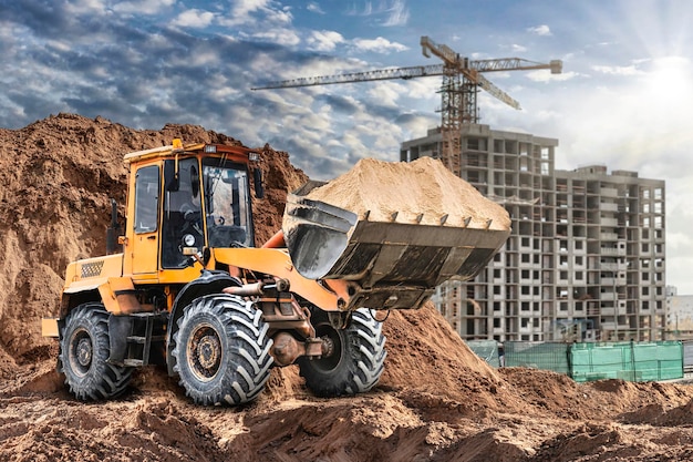 Bulldozer o cargador en un sitio de construcción palas suelo de montaña en un montón Potente cargador de ruedas o bulldozer con un cubo grande en un sitio de construcción Equipos de construcción para movimiento de tierras