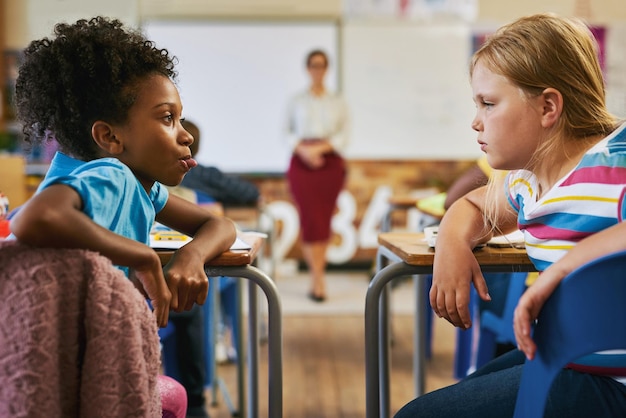 Bullying deve ser monitorado de perto Foto de uma jovem sentada na sala de aula na escola e puxando a língua para o colega