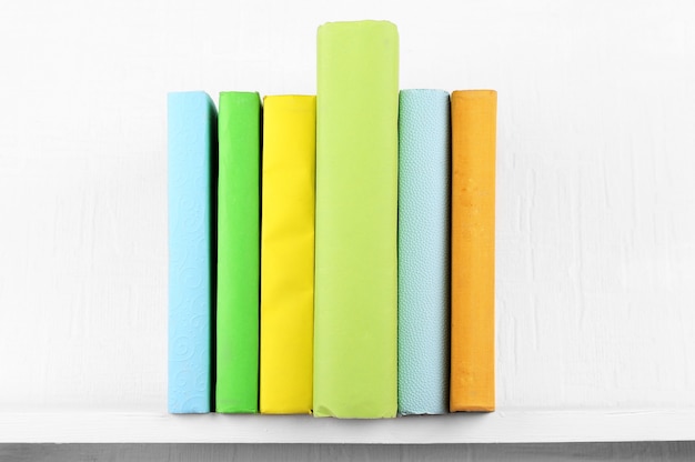Bunt bedeckte Bücher auf Bücherregal und weißer Wand