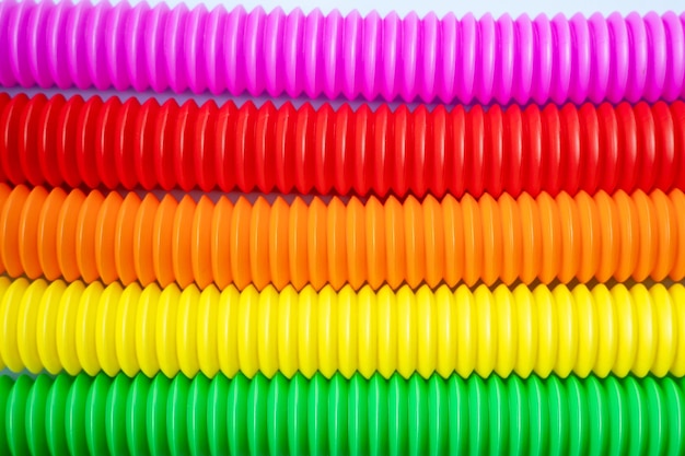 Bunte Anti-Stress-Zappel-Pop-Röhren-Sinnesspielzeug für Kinder auf blauem Hintergrund. Ansicht von oben, flach. Nahaufnahme des kreativen Spiels mit dem beliebten flexiblen hellen Wellrohr aus Kunststoff.