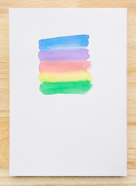 Bunte Aquarellpinselstriche auf weißem Papierblatt mit hölzernem Hintergrund. Nahaufnahme.