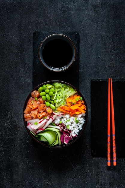 Bunte asiatische trendige Sushi-Poke-Schüssel mit Reisgurken-Lachs-Karotten-Edamame-Bohnen und Sojasauce Draufsicht aus nächster Nähe