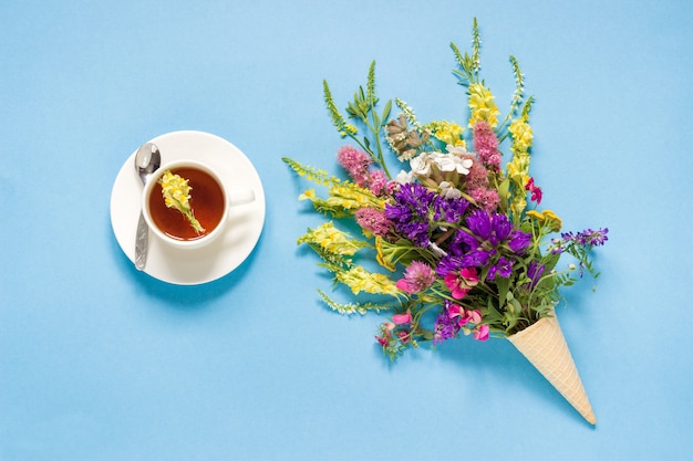 Bunte Blumen des Feldes in der Waffeleiskegel und in der Tasse Tee