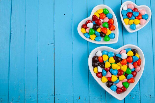 Bunte Bonbons in einem Teller in Herzform auf blauem Holzhintergrund. Valentinstag. Platz für Ihren Text.