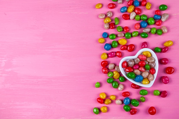 Bunte Bonbons in einem Teller in Herzform auf rosa Holzhintergrund. Valentinstag. Platz für Ihren Text.