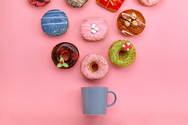 Bunte Donuts mit Zuckerguss und Kaffeetassen auf pastellfarbener Rosenoberfläche. Süße Donuts.