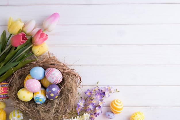 Bunte Eier des glücklichen Ostertages in Nest- und Blumendekoration auf weißem Holz