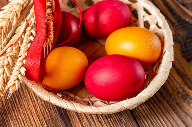 Bunte Eier für Ostern im Strohkorb mit Ähren auf braunem Holz