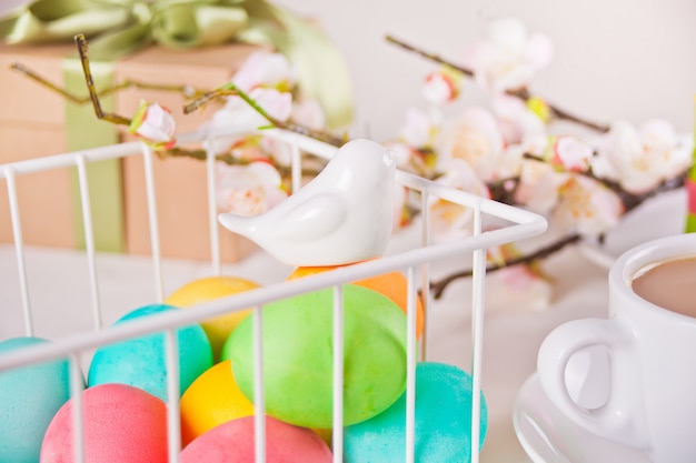 Bunte Eier für Ostertag in einem Korb. Kirschblütenzweig, Tasse Tee und Geschenkbox