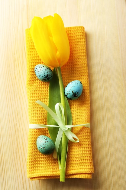 Bunte Eier und Serviette der gelben Tulpe auf Platte auf hölzernem Hintergrund Beschneidungspfad eingeschlossen