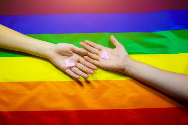 Bunte Flagge der LGBT-Community. Die Hände von zwei Frauen auf Regenbogenhintergrund. Lesben- und Schwulenprobleme. Legalisierung der Ehe für Paare mit homosexueller Orientierung.