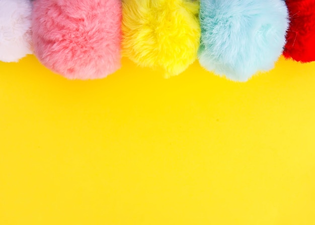 Bunte flauschige Pompons auf hellgelbem Hintergrund. Modedekoration festliche Vorlage. Gestaltungselement für Poster, Banner, Web, Grußkarte.