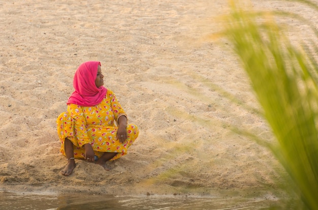 Bunte Frau, die im sandigen Strand sitzt