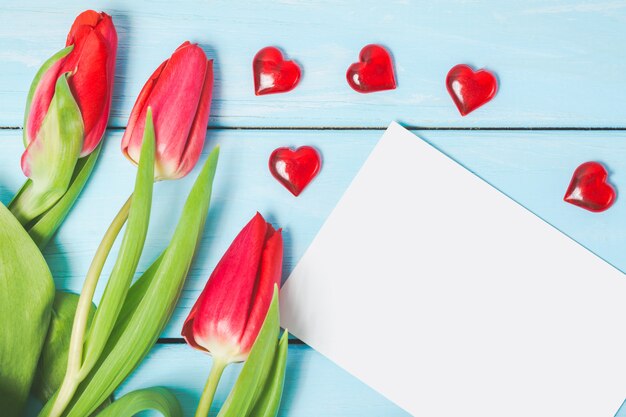 Bunte Frühlingstulpenblumen mit leerem Foto und dekorativen roten Herzen auf hellblauem hölzernem Hintergrund.